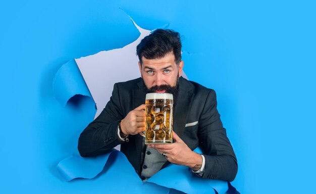 Piwo Oktoberfest i brodaty mężczyzna z ciemnym piwem trzyma piwo rzemieślnicze patrząc przez napoje z papierowej dziury