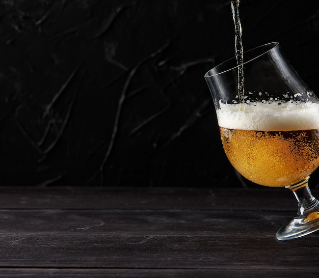 Zdjęcie piwo wlewające się do szklanego drewnianego stołu ciemna ściana