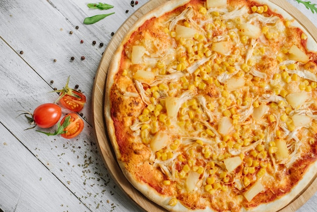 Pizza Americana z mozzarellą, filetem z kurczaka, ananasem i kukurydzą na drewnianym tle