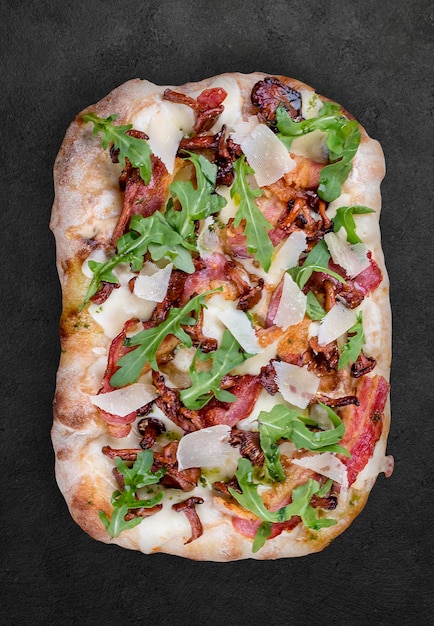 Pizza Carbonara z boczkiem kurki rukola mozzarella parmezan pesto rzymska pizza prostokątna na ciemnym tle