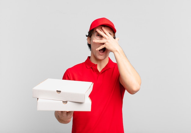 Pizza dostarcza chłopaka, który wygląda na zszokowanego, przestraszonego lub przerażonego, zakrywa twarz dłonią i zerka między palcami