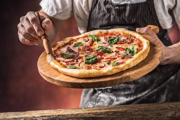 Pizza i szef kuchni. Szef kuchni w restauracji przygotowuje pizzę i ozdabia ją oliwą z oliwek.