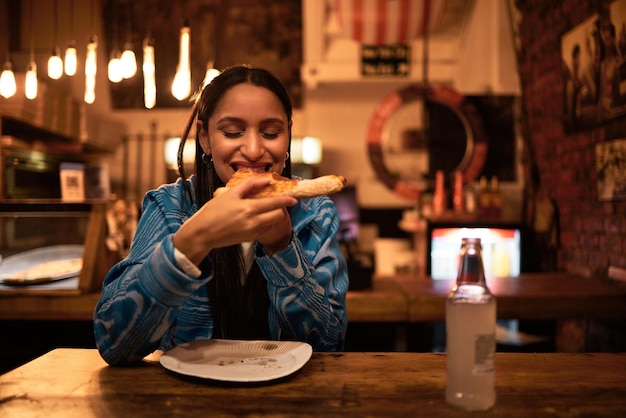 Pizza jedzenie i restauracja, w której młoda kobieta je jedzenie i pije napoje Głodna kobieta je pyszny posiłek w barze w nocy Szczęśliwy i zadowolony smakosz je smaczną kolację w barze