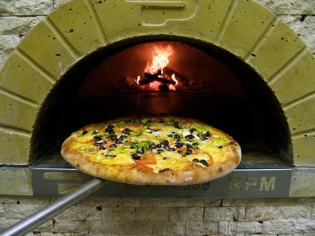 Pizza jest w ceglanym piecu z napisem „lpm” z boku.