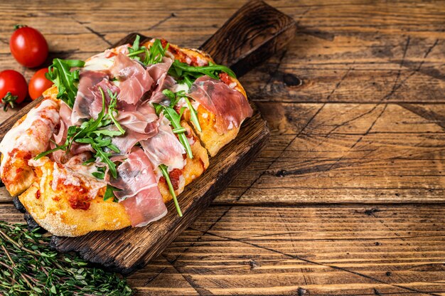 Pizza krojona z szynką parmeńską prosciutto, rukolą i parmezanem na drewnianej desce. drewniane tła. Widok z góry. Skopiuj miejsce.