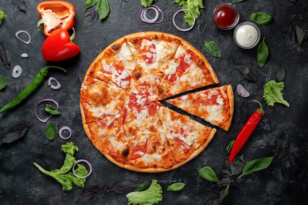 Pizza margarita z ciemnego kamienia z warzywami, papryką, mozzarellą i bazylią. Widok z góry na ciemny kamienny stół