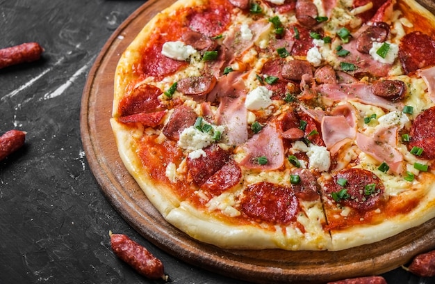 Pizza mięsna z salami, szynką i serem feta na tablicy i na ciemnej powierzchni