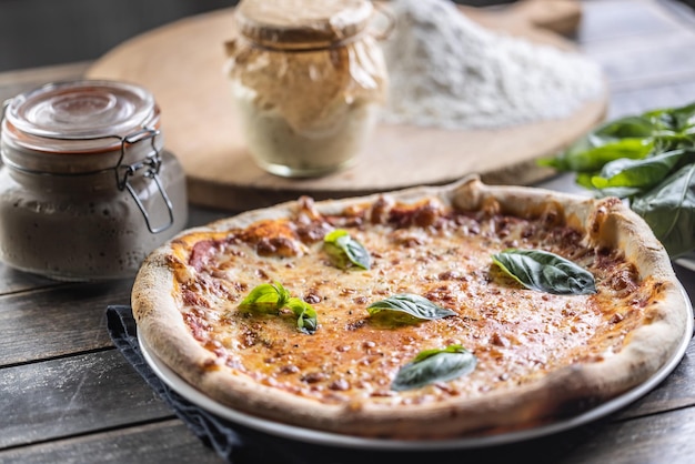 Pizza Napoli z sosem pomidorowym mozzarella i świeżą bazylią w tle mąka i słoik żytniego zakwasu
