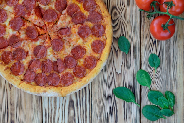 Pizza Pepperoni ze szpinakiem i pomidorami na drewnianym stole. Orientacja pozioma, widok z góry.