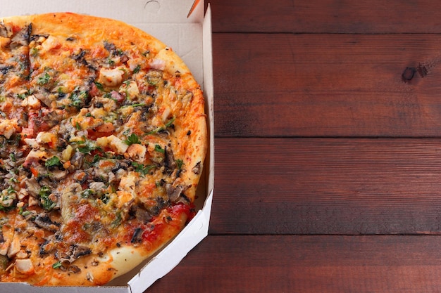 Pizza w kartonowym pudełku na drewnianym tle włoska pizza z kurczakiem, grzybami, zieleniami, serem i sosem