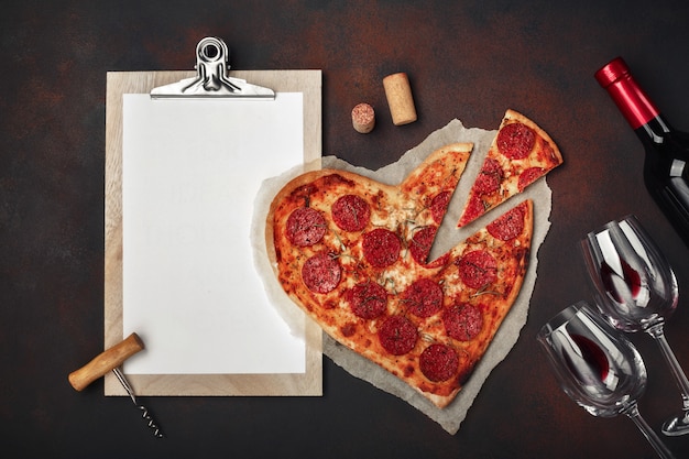 Pizza w kształcie serca z mozzarellą, kiełbasą, butelka wina, dwa kieliszki i tablet na zardzewiałym tle