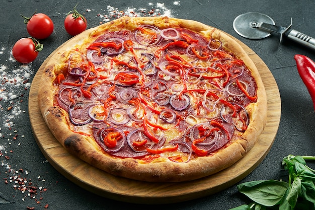 Pizza z dużą ilością dodatków: kiełbasy myśliwskie, cebula, salami, ser i chili. Pizza w składzie ze składnikami na czarnym stole