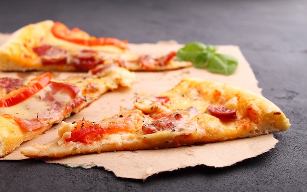 Pizza z kiełbasą, szynką, pomidorem i serem, ozdobiona bazylią i pokrojona na kawałki na pergaminie