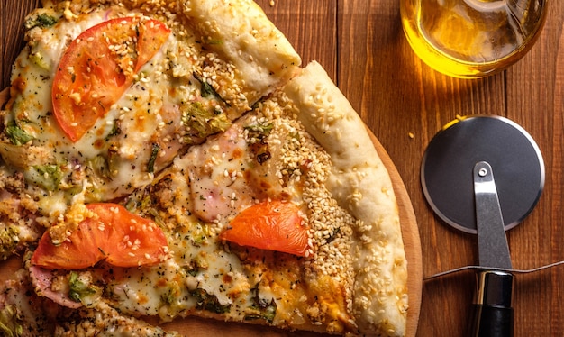 Pizza z serem, pomidorami, szynką i sezamem na desce do krojenia