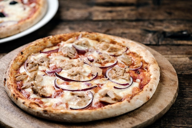 Pizza z tuńczykiem i czerwoną cebulą na drewnianej desce do krojenia