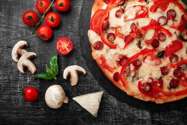 Pizza z wędzonymi kiełbaskami, serem, pieczarkami, pomidorami cherry, papryką i zielenią na kamieniu.