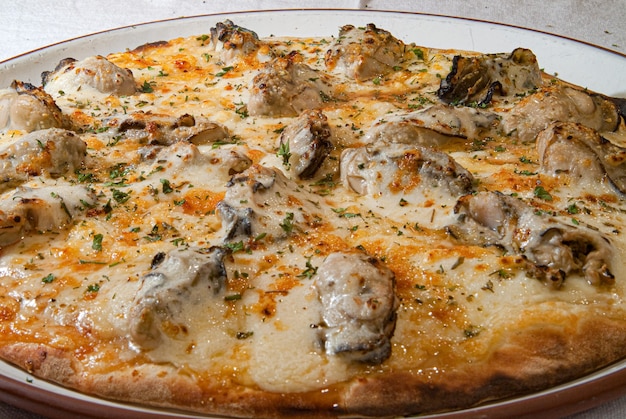 Pizza ze specjalnym smakiem mozzarelli z ostrygami i drobnymi ziołami podana na białym talerzu