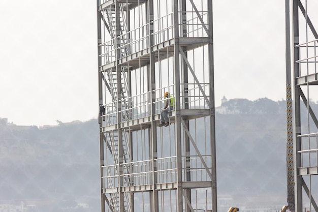 Plac budowy czarny robotnik siedzi na wysokości ramy budynku