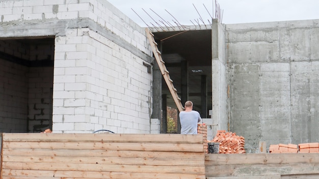 Zdjęcie plac budowy z pracownikami. nowoczesne budynki w budowie za drewnianym ogrodzeniem. roboty budowlane. monolityczny budynek parterowy z betonu i budynków z czerwonej cegły.