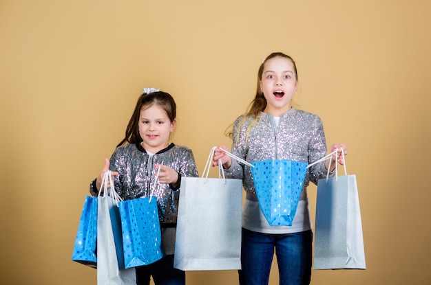 Płać mniej Dziewczyny siostry przyjaciółki z torbami na zakupy beżowe tło Zakupy i zakupy Czarny piątek Wyprzedaż i rabat Dzień zakupów Dzieci trzymają kilka paczek Moda dziecięca Oczekuj więcej