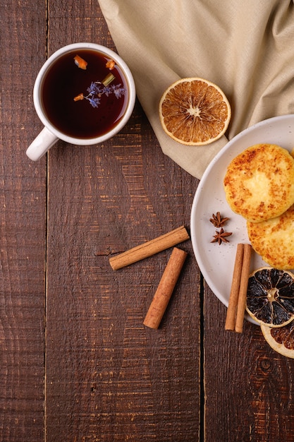 Placki twarogowe z gorącą czarną aromatyczną herbatą, świąteczny nastrój śniadania z anyżem, cynamonem i suszonymi cytrusami na drewnianym tle, widok z góry