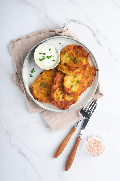 Placki ziemniaczane Smażone domowe placki ziemniaczane lub latkes ze śmietaną i zieloną cebulą w rustykalnym talerzu na białym tle marmurowego stołu Styl rustykalny Zdrowa żywność Widok z góry