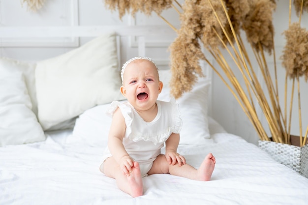 Płaczące małe dziecko na białym łóżeczku w jasnym pokoju noworodek płaczący łzami