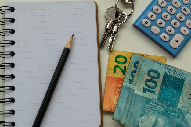 Planowanie wynajmu nieruchomości. Brazylijskie pieniądze, kalkulator, notatnik, ołówek i klucze.