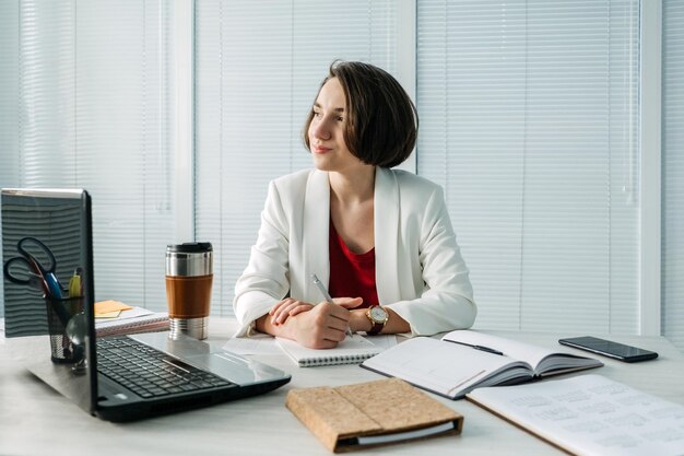 Planowanie zarządzania czasem dla menedżerów właścicieli firm Młody menedżer Businesswoman siedzi przy stole w biurze i robi notatki w dzienniku i kalendarzu