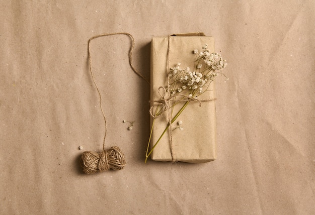 Płaska kompozycja wiosenna z białą gałązką gipsówki na pudełku prezentowym w papierze pakowym kraft i wiązaną kokardką na zmiętym kartonowym tle z miejscem na kopię na reklamę