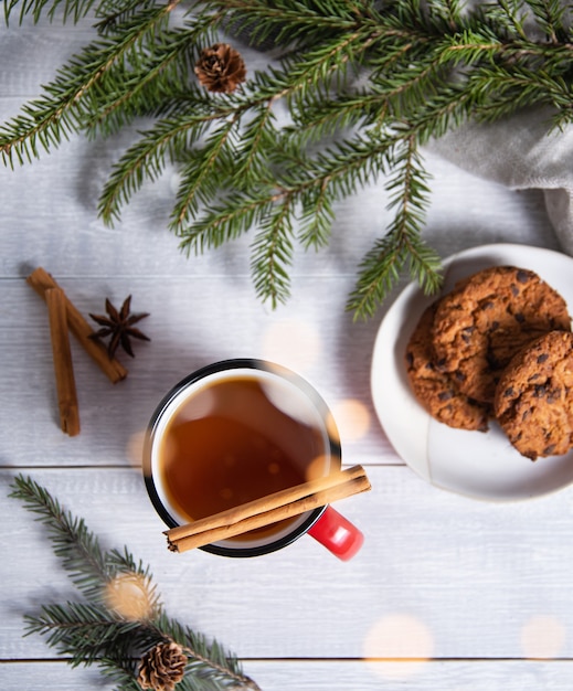 Płaska świecka świąteczna herbata z cynamonem i przyprawami w czerwonym kubku z domowymi ciasteczkami na drewnianym tle z choinką i bokeh. Widok z góry