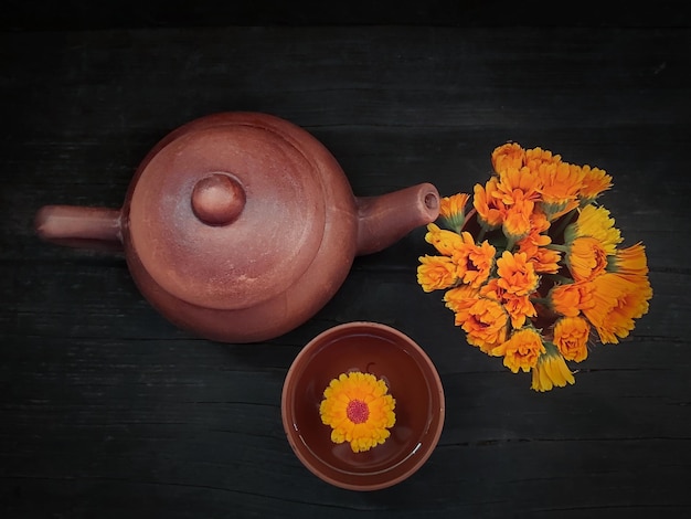 Zdjęcie płaski czajniczek z filiżanką kwiatów nagietka na czarnym drewnianym tle herbata z nagietka