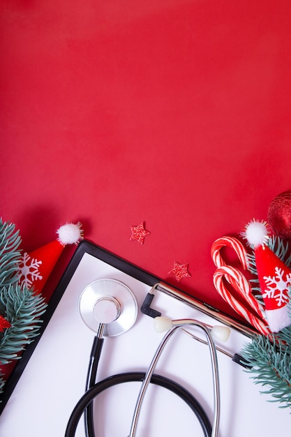 Płaski schowek z medycznym stetoskopem, okularami, choinką na czerwonym tle z miejsca na kopię. Medyczna koncepcja Bożego Narodzenia