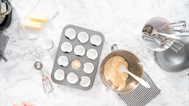 Płaski układanie. Nabieraj ciasto na babeczki do formy do babeczek wyłożonej wkładkami do babeczek, aby upiec babeczki waniliowe.