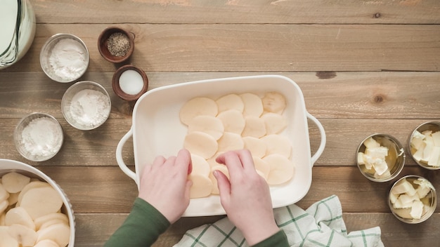 Płaski układanie. Przygotowanie zapiekanych ziemniaków w białej ceramicznej naczyniu do pieczenia.