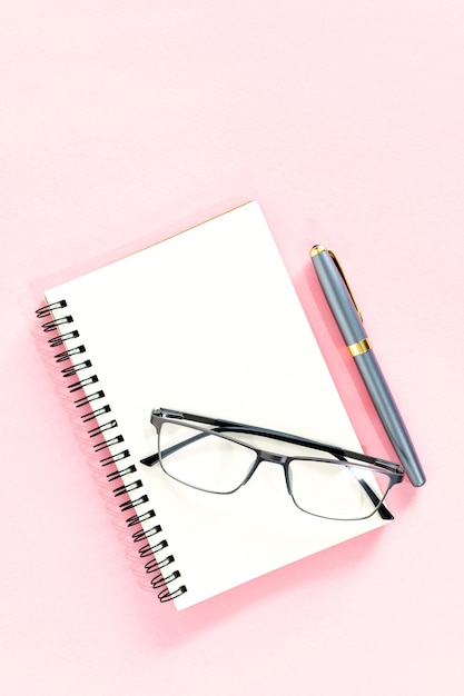 Płaskie ułożenie papeterii z notatnikiem ołówkiem i okularami na jasnoróżowym tle Minimalna przestrzeń do pracy