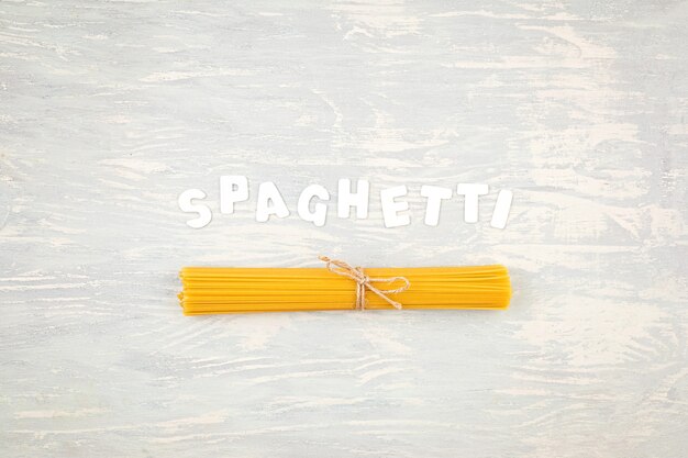 Płaskie ułożenie spaghetti do gotowania włoskiego makaronu na jasnej drewnianej ścianie. Widok z góry na tradycyjną włoską koncepcję kuchni