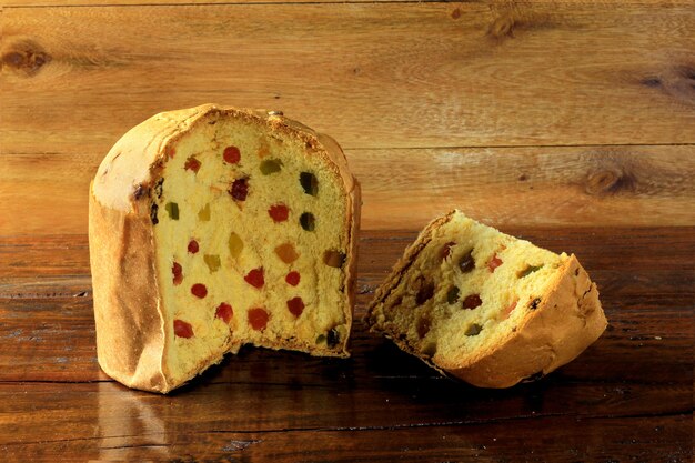 Plasterek Panettone zbliżenie z candied owoc drewnianym stołem. Świąteczne dekoracje. front v