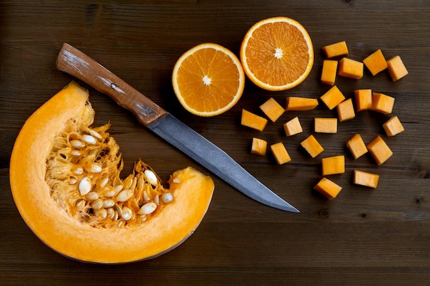 Plasterek świeżej dyni ekologicznej, pokrojone pomarańcze i nóż na ciemnym drewnianym stole. Robienie dżemu