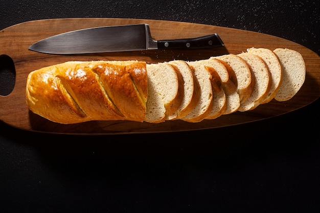 Plasterki bochenka chleba na desce do krojenia i nóż szefa kuchni na czarno