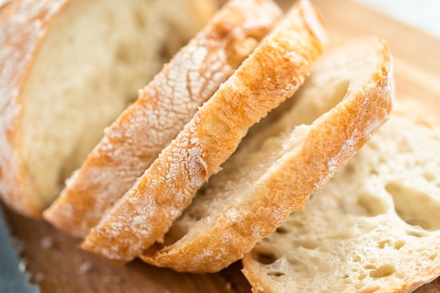 Plasterki świeżego bochenka chleba na drewnianej desce do krojenia.