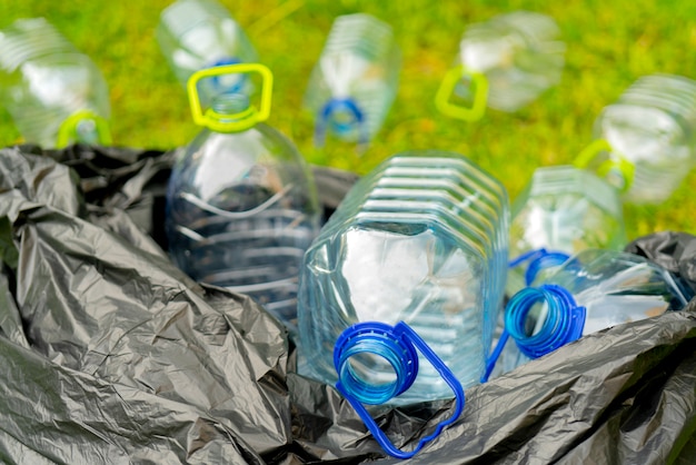 Zdjęcie plastikowe butelki w czarnej plastikowej torbie na śmieci na tle trawy.