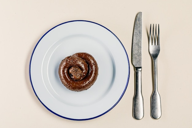 Plastikowe ekskrementy leżą na talerzu między widelcem a nożem zbliżenie Koncepcja nieudolnego kucharza fałszywe wiadomości gówniana restauracja złe jedzenie smak gówna