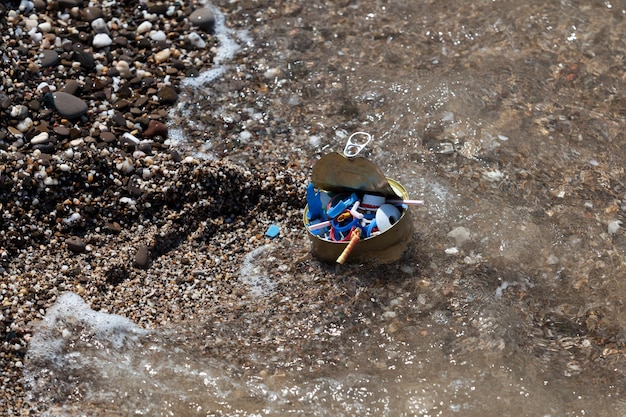 Plastikowe śmieci i blaszane puszki na brzegu morza. Odpady domowe i jednorazowe odpady z tworzyw sztucznych na plaży. Fala morska, mikrodrobiny plastiku w światowym oceanie.