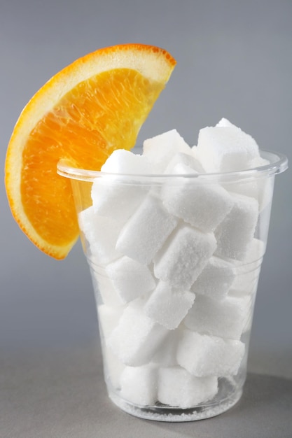 Zdjęcie plastikowe szkło pełne cukru z pomarańczą na szarym tle