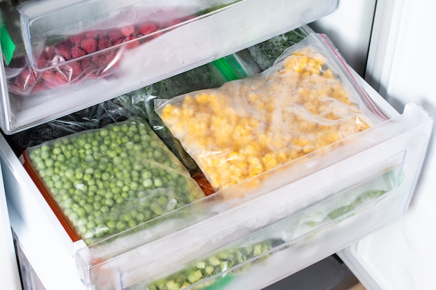 Plastikowe torebki z różnymi mrożonymi warzywami w lodówce.