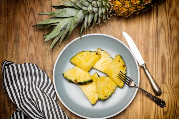 Zdjęcie plastry ananasa na szarym talerzu i na drewnianym tle