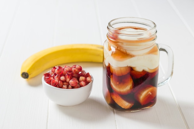 Plastry banana w soku z granatów z jogurtem na białym stole. Przygotowanie smoothie z granatów z bananem.