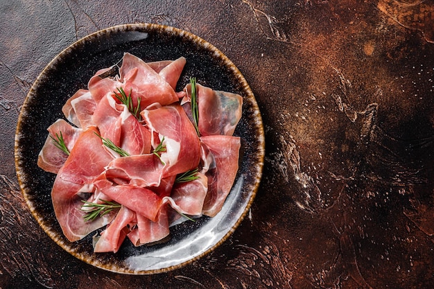 Plastry prosciutto crudo parma lub jamon serrano z rozmarynem na ciemnym tle widok z góry miejsce