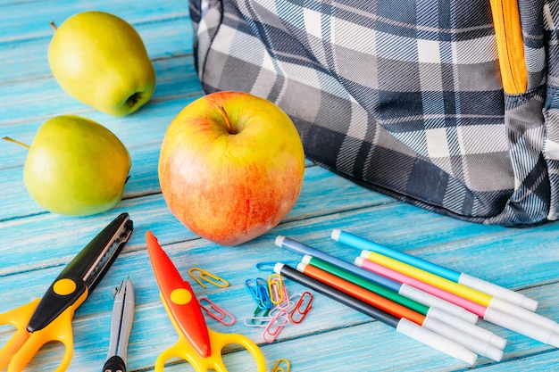 Plecak, jabłko i szkolne dostawy na drewnianym tle